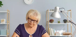 Starsza osoba licząca pieniądze przy biurku z notesem i skarbonką jako symbol przedawnienia długu i analizy zobowiązań